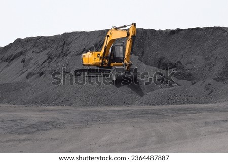 A backhoe - excavating equipment, Digger working on the bulk mountain of coal imported at Dindayal Port Trust, Kandla. Gujarat - India