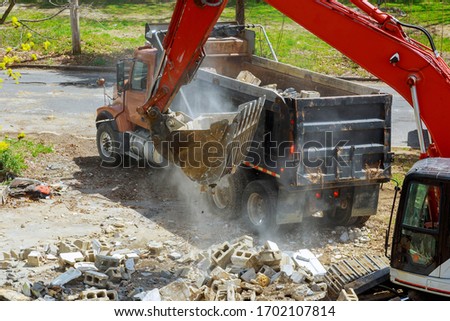 Backhoe excavator scoop loading from building in the construction debris a dump truck
