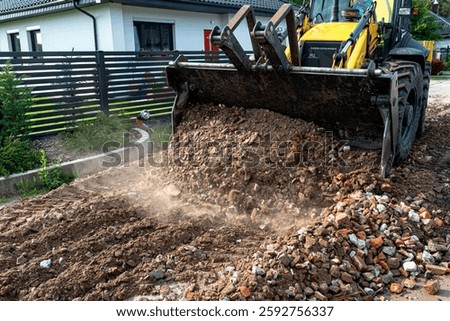 A backhoe loader carries and levels rubble on a dirt road.