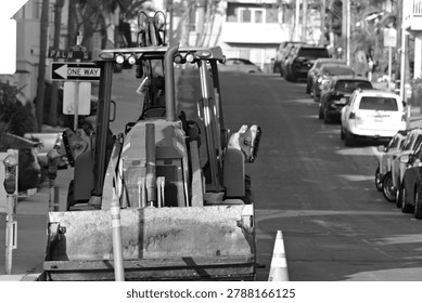 A backhoe loader is parked with cones on an uphill street in Hermosa Beach, California.