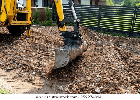 A backhoe loader picks up rubble with a telescopic bucket to level the dirt road.