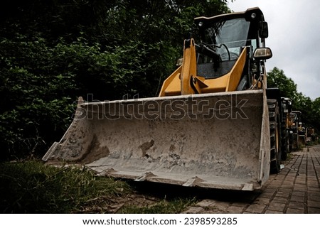 Backhoe loader, trees, paving stones, Tractor parked near the forest. Yellow tractor, excavator - heavy-duty machine.