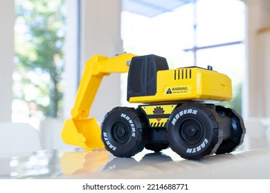 Backhoe Loader, Yellow Construction Toy Vehicle With Articulated Parts Built With Sturdy Plastic Is Placed On A Table.
