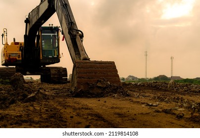 Backhoe Parked At Construction Site After Digging Soil. Closeup Bucket Of Bulldozer. Digger After Work. Earth Moving Machine At Construction Site Of Housing Estate. Digger With Dirt Bucket And Soil.