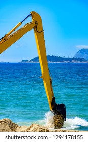 Backhoe removing sand from the beach and throwing in the sea to unclog the passage