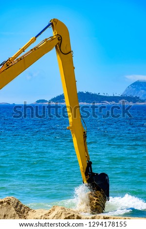 Backhoe removing sand from the beach and throwing in the sea to unclog the passage