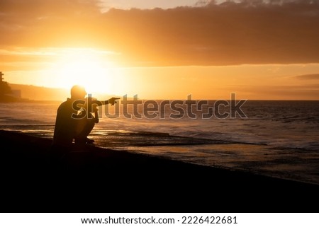 Backlight of a father and his little toddler son watching a sunset in front of the sea in Tenerife, Canary Islands