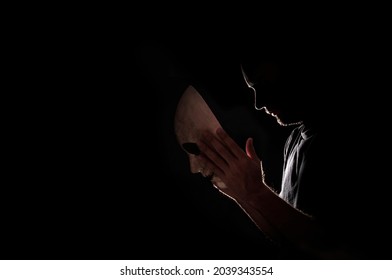 Backlight Of A Man Wearing A Mask. Concept Of Hiding And Mystery. Silhouette. Image Halloween. Black Background With Space For Copying.