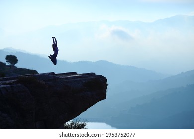 Backlight portrait of a woman silhouette jumping in the top of a cliff on blue landscape