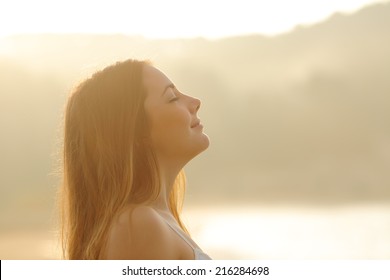 Backlight profile of a woman breathing deep fresh air in the morning sunrise isolated in white above - Powered by Shutterstock