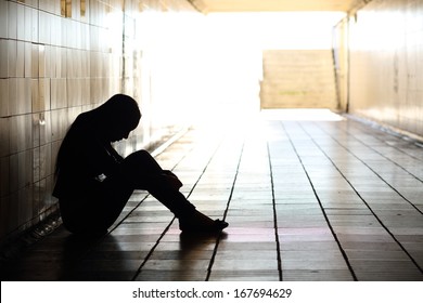 Backlight of a teenager depressed sitting inside a dirty tunnel 