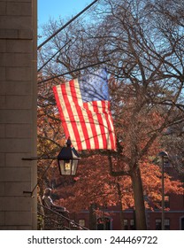 Backlit American Flag Over The John Harvard Statue On A Beautiful Fall Day In Cambridge, MA, USA.