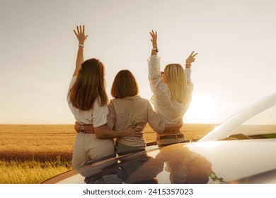 Backlit by a stunning sunset, three friends unite in celebration, sharing a peaceful moment on their scenic road trip - Powered by Shutterstock