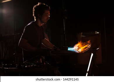 Backlit man with blowtorch shaping glass object