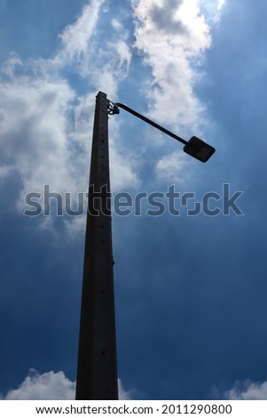 Backlit photograph of LED lamps mounted on tall concrete lampposts. In an outdoor pedestrian area with a dark sky background.
