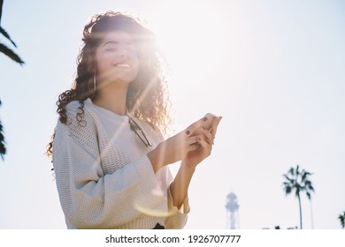 Backlit portrait of funny female tourist 20s posing during travel vacations, happy millennial blogger holding modern smartphone device in hands and smiling at camera enjoying getaway journey