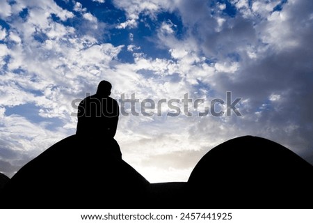 backlit shot of isolated man sitting at wall watching sunset with dramatic sky at dusk