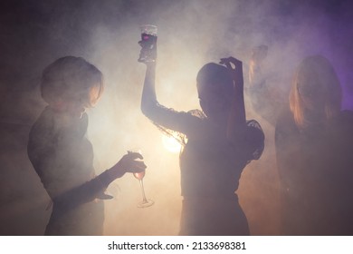 Backlit Shot Of Young Women Dancing At Party, Elegant Silhouettes In Smoky Club