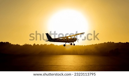 Backlit silhouette of a cessna plane outlined with the sun just behind it flying low with the sea water below illuminated by the golden light of sunset and trees and vegetation in the background