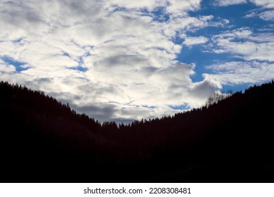 Backlit Silhouette Trees In The Mountain With Blue Sky With Clouds