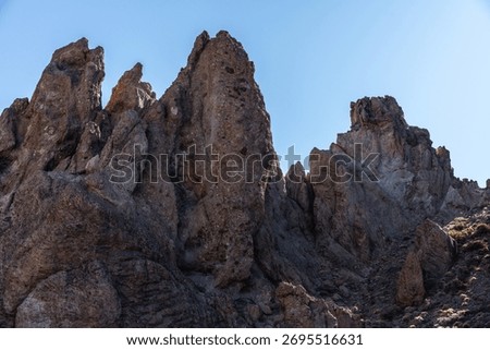 Backlit towering rock formations of Roques de Garcia above pahoehoe lava field with sparse yellow shrubs in Tenerife