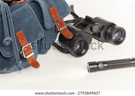 Backpack, binoculars, flashlight in close-up against a white background.