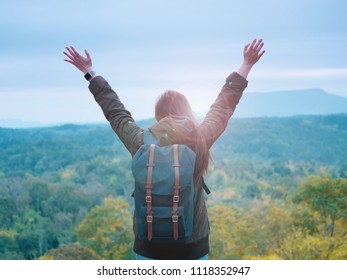 backpack and camping concept from backside of long hair woman in warm cloth with her bag travel, relax, happy  and see to forest and mountain in morning after sunrise