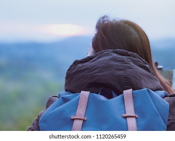 backpack and camping concept from backside of long hair woman in warm cloth with her bag travel, relax, happy  and see to forest and mountain in morning after sunrise