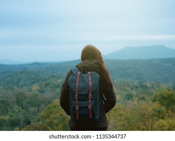 backpack and camping concept from backside of long hair woman in warm cloth with her bag travel, relax, happy  and see to forest and mountain in morning after sunrise