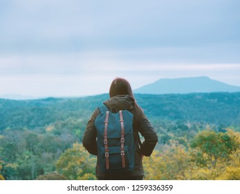 backpack and camping concept from backside of long hair woman in warm cloth with her bag travel, relax, happy  and see to forest and mountain in morning after sunrise
