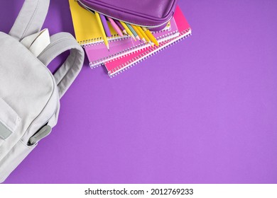 Backpack with colorful school supplies on purple background. Back to school. Flat lay, top view, copy space