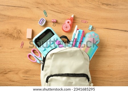 Backpack with colorful school supplies on wooden table, top view. Back to school concept.