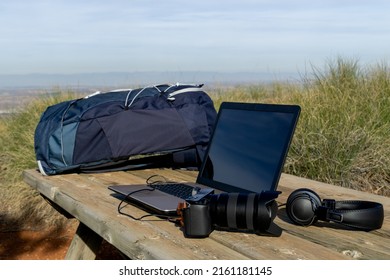 Backpack, computer, camera and headphones on a table in the wilderness - digital nomad concept