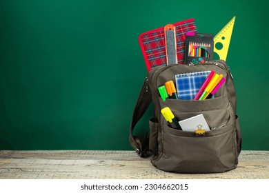 Backpack with different colorful stationery on table. Green background. Back to school - Shutterstock ID 2304662015