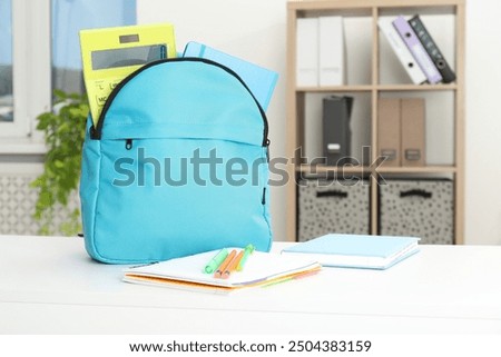 Backpack and different school stationery on white table indoors