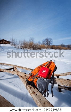 A backpack and first aid kit rest on a wooden fence under the freezing winter sky, overlooking the snowcovered slope. The tranquil landscape is perfect for outdoor recreation