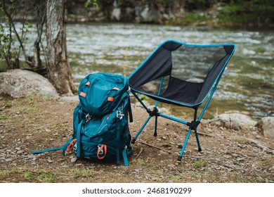 Backpack and a foldable chair set by a river, reflecting nature and adventure. Perfect for hiking, camping, or exploring the outdoors. High-quality gear in a scenic natural setting. - Powered by Shutterstock