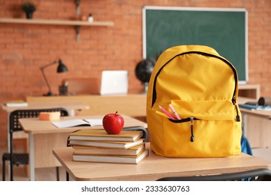 Backpack with fresh apple and books on desk in classroom - Powered by Shutterstock