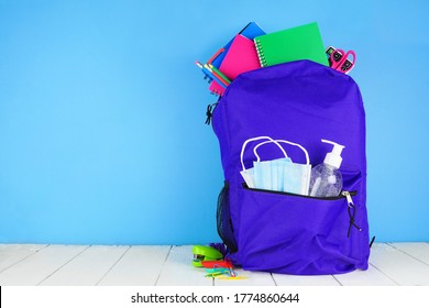 Backpack Full Of School Supplies And COVID 19 Prevention Supplies. Blue Background. Back To School During Pandemic Concept.