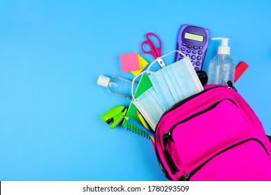 Backpack Full Of School Supplies And COVID 19 Prevention Items. Top View, Spilling Onto A Blue Background. Back To School During Pandemic Concept.