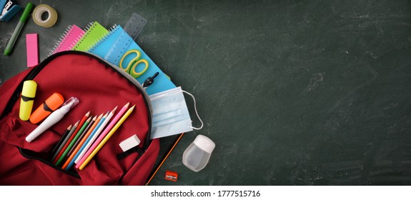 Rucksack voll Schulbedarf auf grüner Tafel mit Schutzmaske und hydroalkoholischem Gel mit Leerraum, um die Draufsicht zu schreiben.