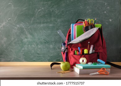 Backpack Full Of School Supplies On Wood Table And Green Blackboard With Blank Space For Writing Front View