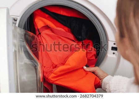 Backpack inside washing machine drum. Orange backpack during cleaning cycle. Household laundry concept with appliance. Domestic routine of washing bag. Hygiene care and cleaning process at home.