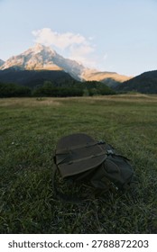 Backpack lying on green grass in front of a mountain with clear sky. Concept of hiking, nature, adventure, and outdoor lifestyle during daytime.