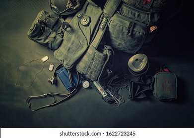 The backpack of a military medic stands on a green background. Around lies a first aid kit and various doctor tools. View from above. Mixed media
