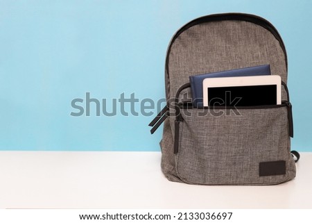 Backpack with notebook and tablet in pocket on wooden table. Blue wall background. Back to school concept. Educational banner design. 