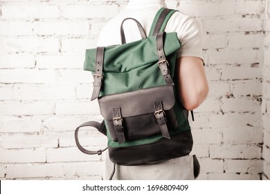 Backpack on man back on wall white brick background. Street urban style black green color. Close up leather bag