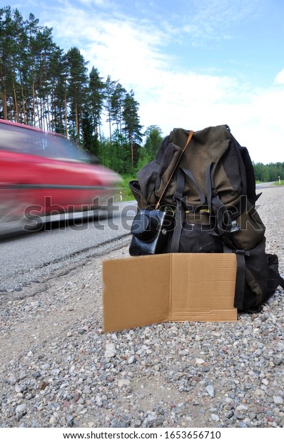 Backpack on the side of the road with blank\
cardboard sign