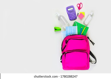 Backpack With School Supplies And COVID 19 Prevention Items. Top View, Spilling Onto A White Background. Back To School During Pandemic Concept.