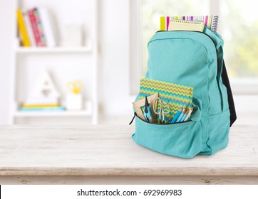 Backpack with school supplies on table over blurred educational interior